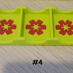 May include: A lime green card holder with three compartments, each featuring a red flower design. The number "#4" is printed in black at the bottom. The holder is made of a solid material.