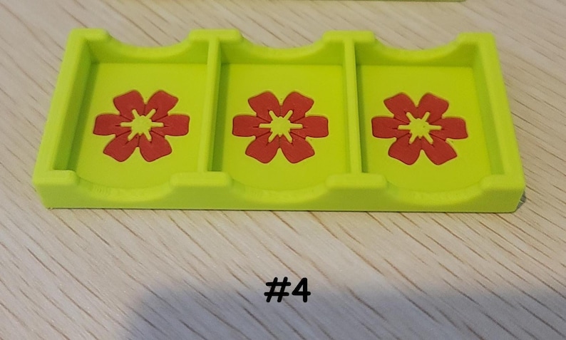 May include: A lime green card holder with three compartments, each featuring a red flower design. The number "#4" is printed in black at the bottom. The holder is made of a solid material.