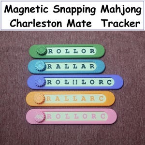 May include: A collection of colorful, magnetic Mahjong Charleston Mate trackers. Each tracker is a different color, including green, blue, purple, orange, and pink, with white lettering. The text "Magnetic Snapping Mahjong Charleston Mate Tracker" is at the top.