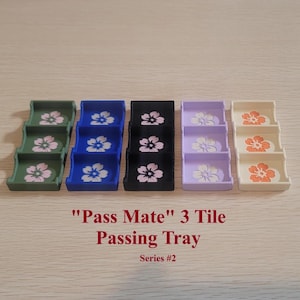 May include: A set of five colorful "Pass Mate" 3 Tile Passing Trays, each with a floral design. The trays are in shades of green, blue, black, lavender, and cream. The text "Pass Mate" 3 Tile Passing Tray Series #2" is printed below the trays.