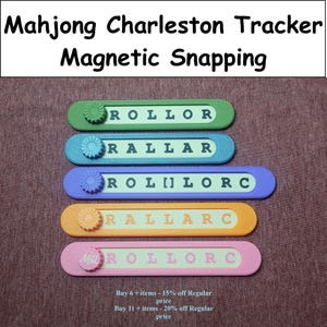 May include: Five rectangular Mahjong Charleston trackers with magnetic snapping sliders in green, blue, purple, orange, and pink. Each tracker features a central track with printed text including ROLLOR, RALLAR, ROL[]LORC, RALLARC, and ROLLORC.