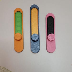 May include: Three colorful nail files. The files are orange, blue, and pink, each with a different colored interior. Each file has a textured, round knob at the base. The files are designed for nail care.