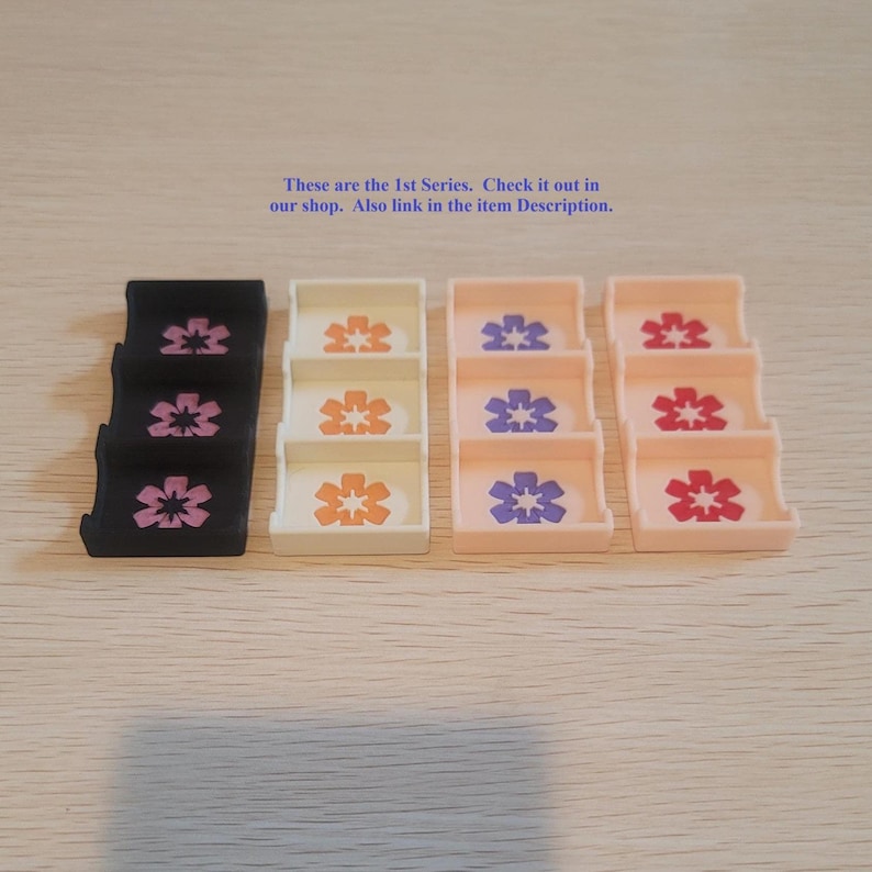 May include: Four rectangular organizers with three compartments each, featuring a six-petaled flower icon in each section. Colors include black, white, light peach, and pale pink. Text reads: These are the 1st Series. Check it out in our shop.