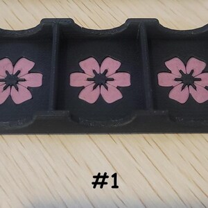 May include: A black, three-compartment tray with pink flower designs. The tray has curved cutouts and is made of a solid material. The number "#1" is printed in black at the bottom of the image.