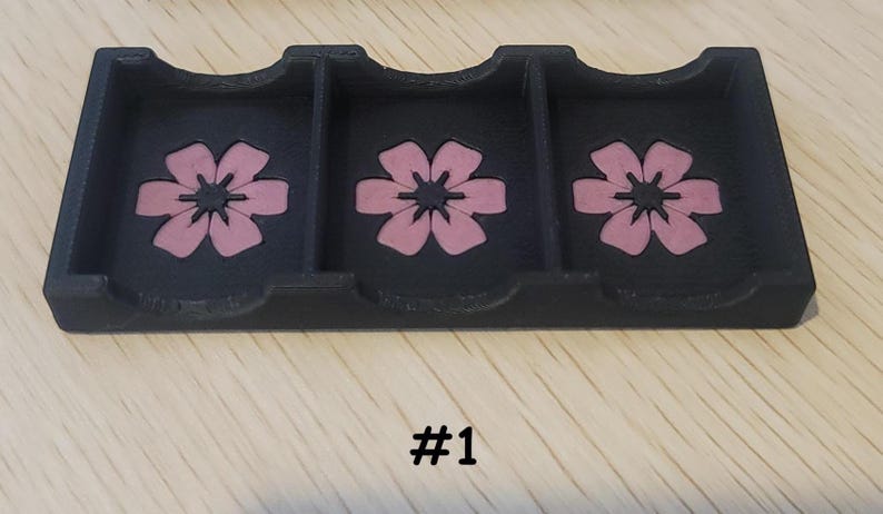 May include: A black, three-compartment tray with pink flower designs. The tray has curved cutouts and is made of a solid material. The number "#1" is printed in black at the bottom of the image.
