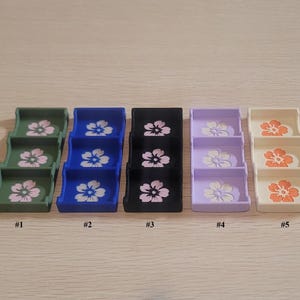 May include: Five miniature, three-tiered display stands in various colors: green, blue, black, lavender, and cream. Each stand features a floral design on each tier. The stands are numbered from one to five.