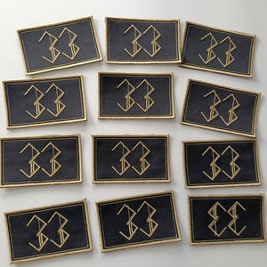 Peut inclure: Plusieurs écussons rectangulaires noirs avec des bordures dorées brodées. Chaque écusson présente le chiffre "33" dans une police dorée stylisée. Les écussons sont disposés sur une surface blanche.