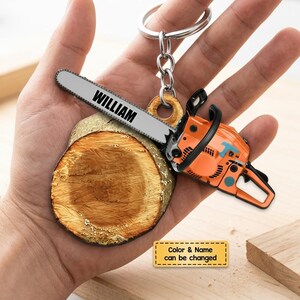 May include: A keychain featuring a miniature orange chainsaw and a wooden log slice. The chainsaw has a silver blade with the name "WILLIAM" printed on it. The keychain also includes a small tag that says "Color & Name can be changed".