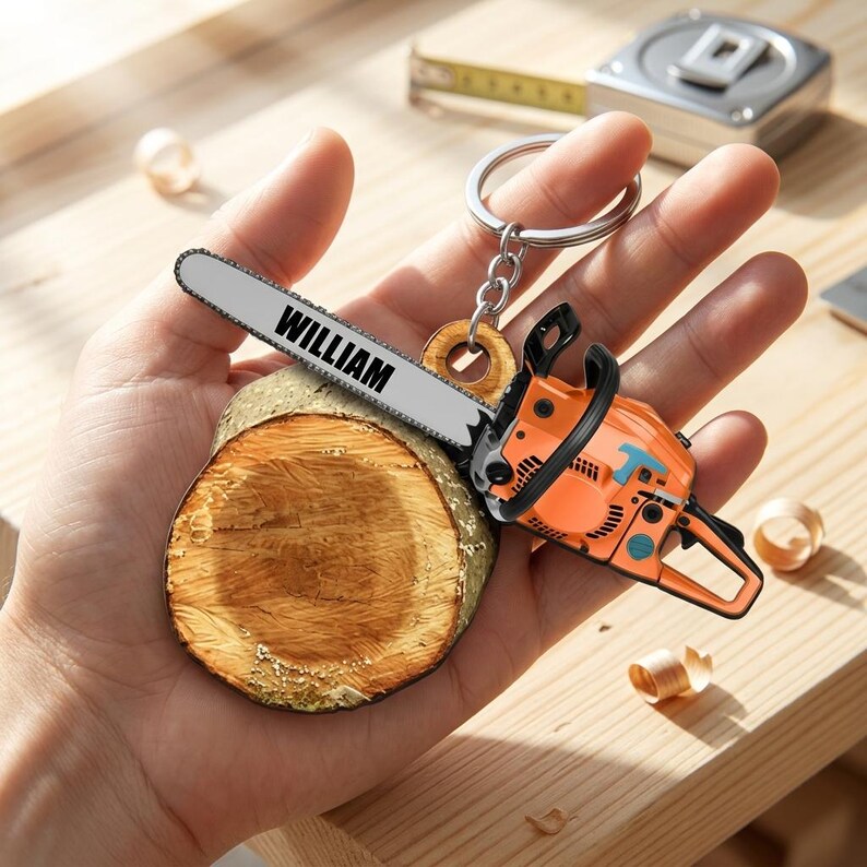 May include: A keychain featuring a miniature chainsaw and a wooden log slice. The chainsaw is orange and black with the name "WILLIAM" printed on the blade. The keychain is attached to a silver ring.