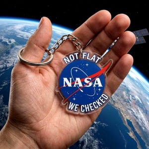 May include: A clear acrylic keychain featuring the NASA logo with the text "NOT FLAT WE CHECKED". The keychain has a silver metal ring and chain. The background shows a view of Earth from space.