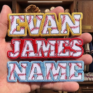 May include: Three rectangular embroidered patches featuring white letters with red baseball stitching patterns. The top patch has gold borders and reads EVAN, the middle patch has red borders and reads JAMES, and the bottom patch has light blue borders and reads NAME.