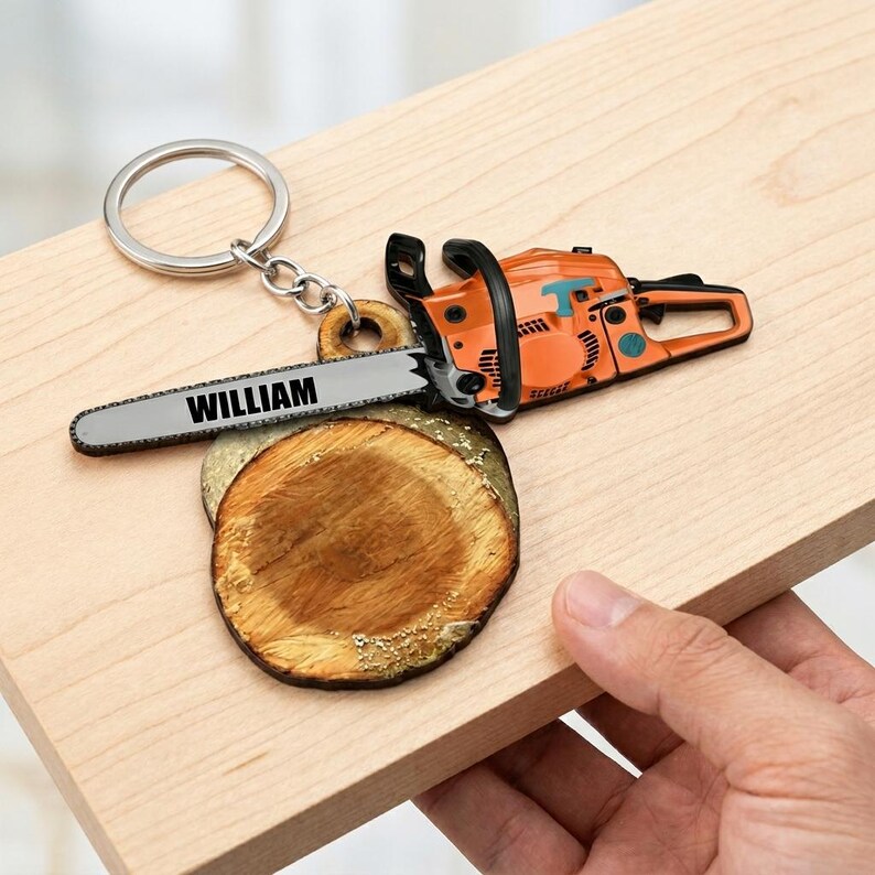 May include: An orange and black chainsaw keychain with the name "WILLIAM" on the blade. The keychain includes a silver ring and a small wooden slice. The chainsaw is detailed with blue accents and a black handle.