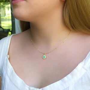 May include: A gold chain necklace with a small sun pendant featuring a turquoise gemstone in the center.