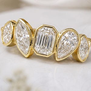 May include: A yellow gold ring featuring five bezel-set diamonds in a row. The center stone is an emerald-cut diamond, flanked by two marquise-cut diamonds and two pear-cut diamonds on the outer edges, all set in a polished gold band.