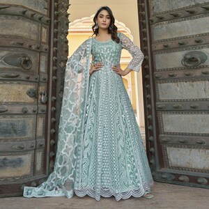 Può includere: Un abito lungo verde chiaro con intricati dettagli in pizzo bianco. L'abito presenta maniche lunghe e trasparenti e uno scialle abbinato. L'abito ha un corpetto aderente e una gonna ampia, perfetto per eventi formali.