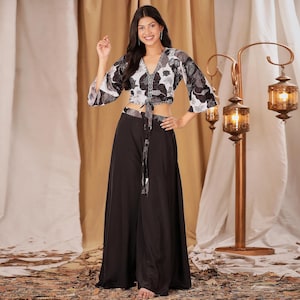 May include: A two-piece outfit comprising a floral print crop top and wide-leg black trousers. The top has a V-neck and tie closure. The trousers are high-waisted and flowing. The floral print includes shades of grey and white.