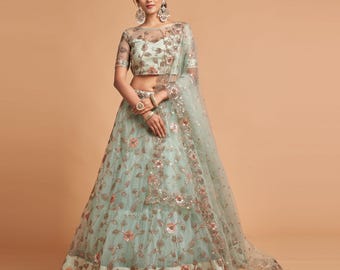 May include: A light blue lehenga with floral embroidery and sequin embellishments. The outfit includes a sheer top with short sleeves and a matching dupatta. The skirt has a flared silhouette, and the overall design is elegant and festive.