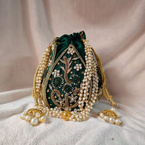 Könnte beinhalten: Eine dunkelgrüne Beuteltasche mit Kordelzug, aufwendiger Goldstickerei und weißen Perlenakzenten. Die Tasche hat Blumen- und Blattmuster, eine goldene Kette und Perlenquasten. Die Tasche ist aus einem samtartigen Material.