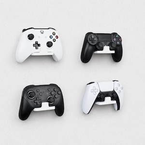 May include: Four video game controllers mounted on white wall brackets. The top left is a white Xbox controller, the top right is a black PlayStation controller, the bottom left is a black Pro controller, and the bottom right is a white PlayStation controller.