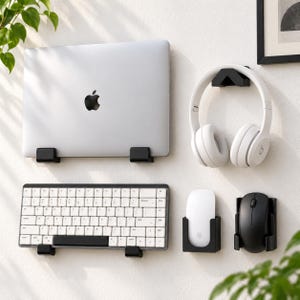 May include: A set of black wall-mounted organizers holding a silver laptop, white wireless keyboard, white over-ear headphones, a white computer mouse, and a black computer mouse. Each device is secured in its own dedicated black plastic mount.
