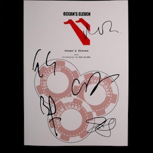Op de afbeelding: Een wit papier met de titel "Ocean's Eleven" in zwart en rood, samen met handtekeningen. De tekst "2001" en "Screenplay by Ted Griffin" zijn ook zichtbaar. De afbeelding bevat casino chip ontwerpen.