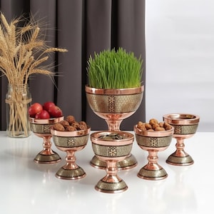 May include: A set of copper-colored serving bowls with intricate patterned designs. The bowls are of varying sizes and shapes, some holding fruits, nuts, and greenery. The set includes a large centerpiece bowl with tall grass.