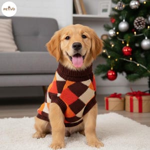 Op de afbeelding: Een golden retriever pup draagt een bruine, oranje en crèmekleurige trui met een ruitpatroon. De hond zit op een wit tapijt met een kerstboom en cadeaus op de achtergrond. De trui heeft een coltrui.