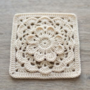 Può includere: Un motivo quadrato all'uncinetto di colore crema chiaro caratterizzato da un design floreale centrale con petali a strati. Il motivo passa da un centro floreale circolare a un bordo quadrato con complessi punti traforati e un bordo solido.