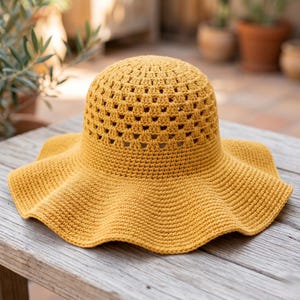 Peut inclure: Chapeau de soleil en crochet jaune moutarde avec un large bord ondulé. Le chapeau présente un motif ajouré sur la couronne. Le chapeau est posé sur une surface en bois vieilli. C'est un article fait à la main.
