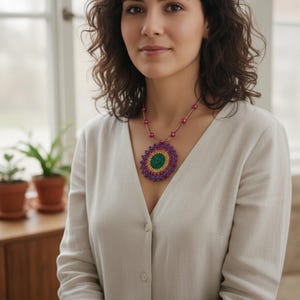 May include: A vibrant crochet necklace with a large pendant. The pendant has a green centre, encircled by yellow and purple crochet. The necklace is strung with pink beads.