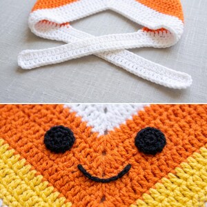 May include: A crocheted hat featuring a candy corn design with horizontal stripes of white, orange, and yellow. The hat includes two white crocheted ties and a face composed of two round black eyes and a curved black mouth stitched onto the orange section.