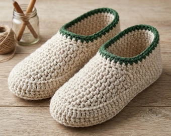 Può includere: Un paio di pantofole all'uncinetto fatte a mano, color crema, con un bordo verde scuro. Le pantofole sono realizzate con un filato spesso e hanno un aspetto strutturato. Sono visibili anche uncinetti e spago.