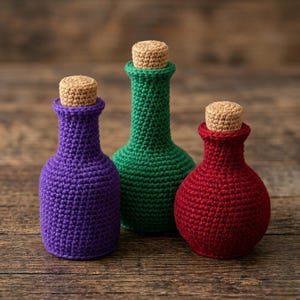 May include: Three crocheted bottles in purple, green, and red, each with a cork stopper. The bottles are arranged on a wooden surface. The crochet work is visible, and the bottles have a handmade appearance.