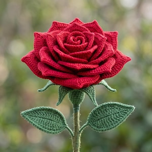 Puede incluir: Una rosa tejida a mano en crochet con pétalos de color rojo vibrante dispuestos en un patrón floreciente y superpuesto. La flor se sostiene sobre un tallo verde con dos hojas verdes texturizadas y detalladas a los lados y un cáliz verde.