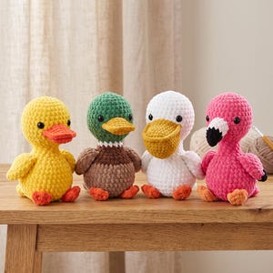 May include: Four crocheted plush toys featuring a yellow duck with an orange beak, a mallard duck with a green head and brown body, a white pelican with a yellow beak, and a pink flamingo with a black and white beak, all with black eyes.