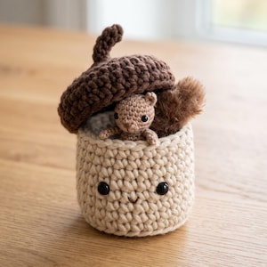 May include: A crocheted acorn-shaped container in cream and dark brown yarn. The base is cream with two black bead eyes and a small stitched mouth. A dark brown crocheted acorn cap sits on top, housing a small, light brown crocheted squirrel figure.