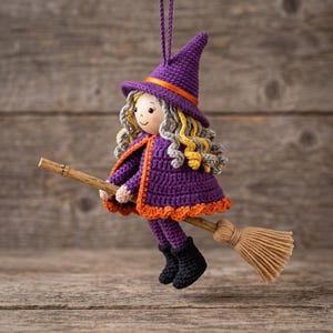 May include: A crocheted witch ornament featuring a purple pointed hat with an orange band, gray and yellow curly hair, and a purple cape with orange trim. The figure holds a wooden broomstick with tan bristles and wears black crocheted boots.