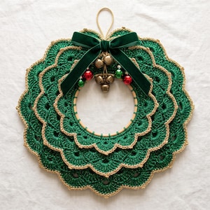 Peut inclure: Une couronne en crochet circulaire avec des bords festonnés vert foncé superposés et une bordure dorée. Un nœud en ruban de velours vert foncé est attaché au sommet, agrémenté de petites clochettes dorées et de boules rouges et vertes.