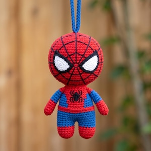 Peut inclure: Une poupée Spider-Man en crochet avec un corps en fil rouge et bleu, un motif de toile noire sur la tête et un emblème d'araignée noire sur la poitrine. La poupée a de grands yeux blancs avec des contours noirs et une boucle de suspension bleue.