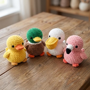 Puede incluir: Cuatro pequeños animales de peluche tejidos a ganchillo, de forma redonda, dispuestos en fila. El conjunto incluye un pato amarillo, un ánade real marrón y verde, un pelícano blanco con pico amarillo y un flamenco rosa con pico negro y blanco.