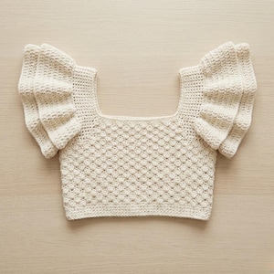 Peut inclure: Haut en crochet de couleur crème avec une encolure carrée et des manches à volants. Le corps du haut présente un motif texturé en forme de losange. Le haut est fait d'une fibre naturelle douce et convient aux températures chaudes.