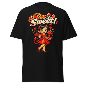 Puede incluir: Camiseta negra con una ilustración de una chica diablo sosteniendo una manzana caramelizada. El gráfico incluye el texto "Sin So Sweet!" en una fuente juguetona, con llamas y corazones. La chica está vestida de rojo, con cuernos y cola.