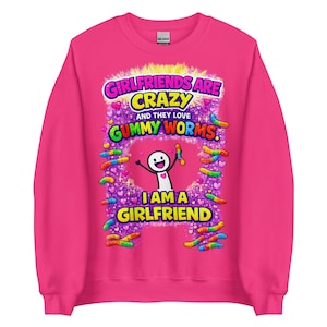 Könnte beinhalten: Ein leuchtend pinkfarbenes Sweatshirt mit dem Text "Girlfriends are Crazy and they love Gummy Worms. I am a Girlfriend." Das Design umfasst bunte Gummibärchen und eine Strichmännchenfigur, die einen Gummibärchen hält.