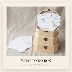 May include: A light-colored wooden box with three stacked octagonal compartments and metal latches. Inside the top section are white cards with black text reading "HERE IS A what to do BOX FOR YOU" and "Stage One". More white cards lie beside the box.