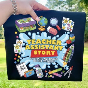 May include: Black t-shirt with a colorful graphic design featuring school-related illustrations and the text "TEACHER ASSISTANT STORY TO INFINITY AND BEYOND FOR OUR STUDENTS." The design includes a globe, rocket, and school supplies.