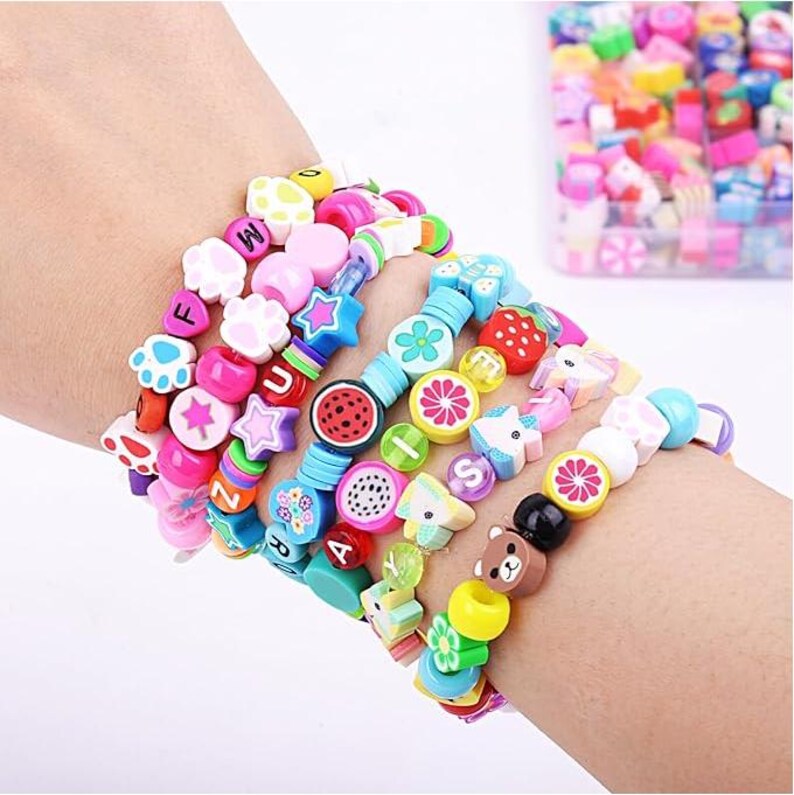 May include: A collection of multi-colored beaded bracelets featuring various shapes including paw prints, stars, flowers, and fruit slices. The beads are made of polymer clay and include letters and geometric forms in bright shades of pink, blue, yellow, and green.