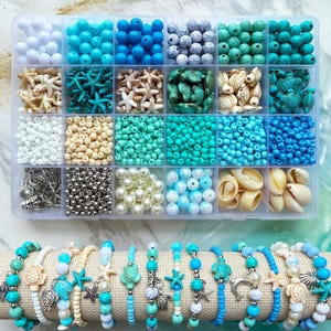 May include: A clear plastic organizer filled with various beads, shells, and charms in shades of blue, white, and beige. Below, several beaded bracelets with sea-themed charms are displayed on a beige fabric roll.