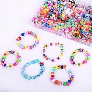 May include: A clear plastic storage container filled with assorted colorful polymer clay beads in various shapes, including letters, fruits, and animals, alongside five finished elastic bracelets made from these same multi-colored beads.