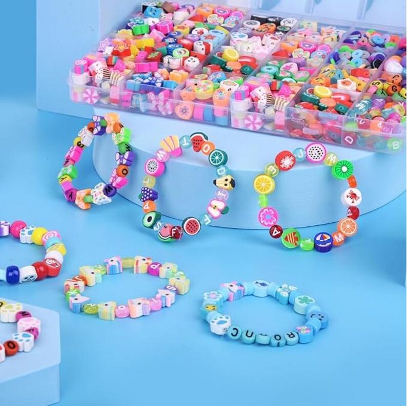 May include: A collection of colorful bracelets made from small polymer clay beads in various shapes, including fruits, letters, and geometric patterns, displayed alongside a clear plastic storage container filled with assorted loose beads.