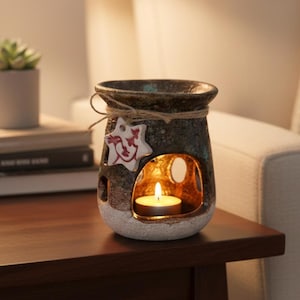 May include: A ceramic essential oil diffuser with a teal and brown speckled finish. It features a star-shaped tag and a small opening to hold a lit tea light candle. The diffuser sits on a dark wooden table.